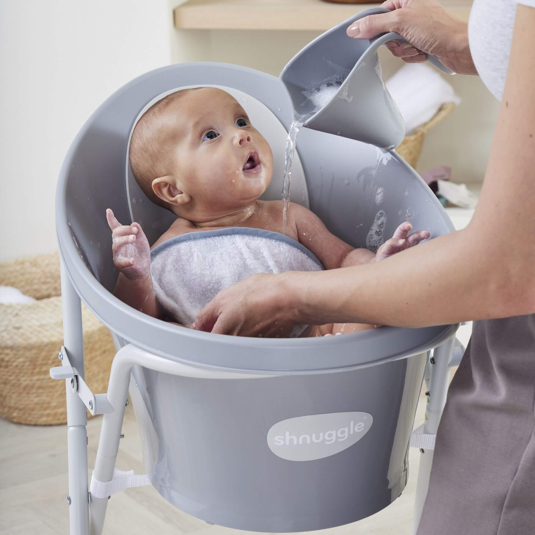 Baby being bathed in a Shnuggle baby bath seat with water being poured over them.