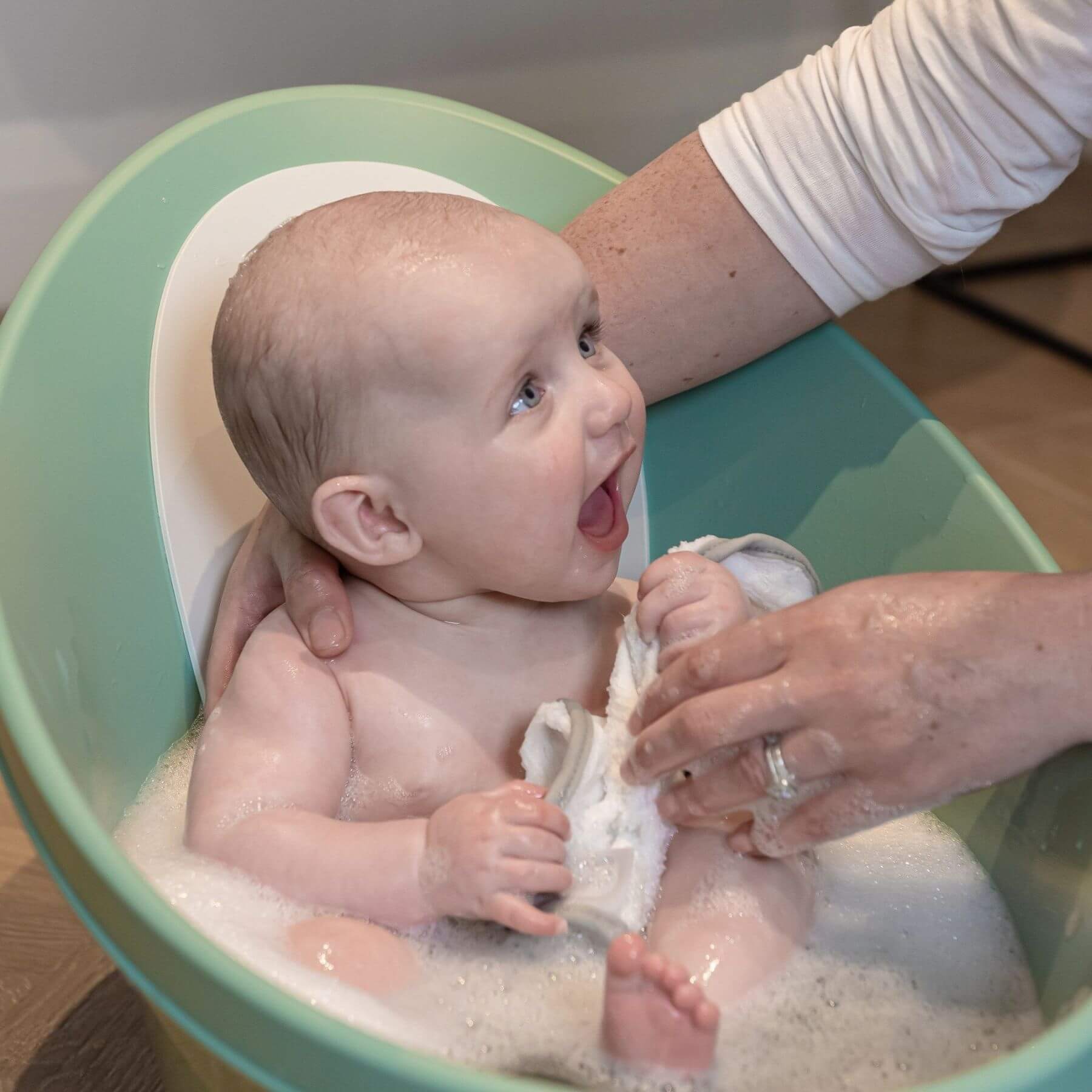 Baby being bathed in Shnuggle Bath with a person assisting