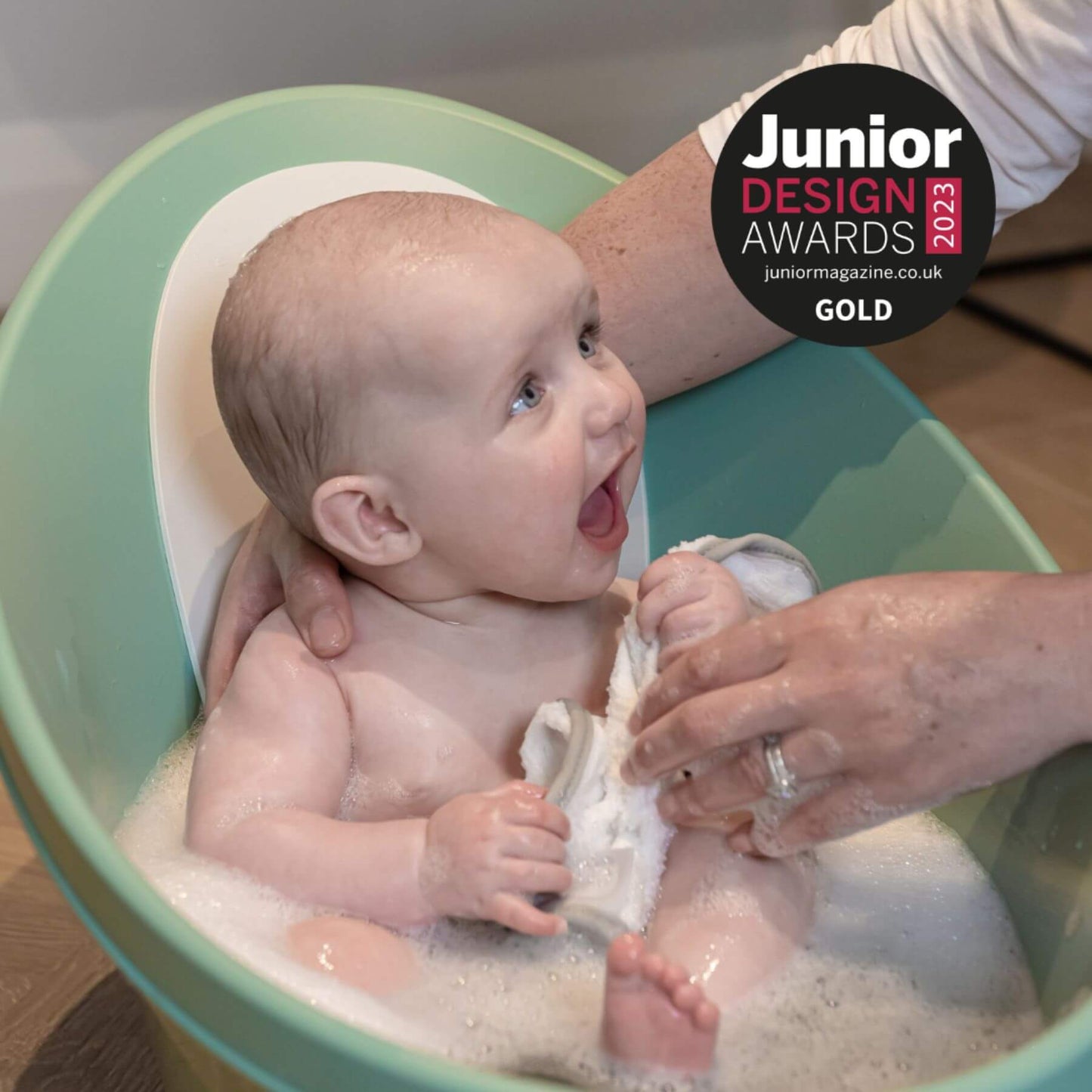 Baby being bathed in Shnuggle Bath with a person, featuring the Junior Design Awards 2023 logo.