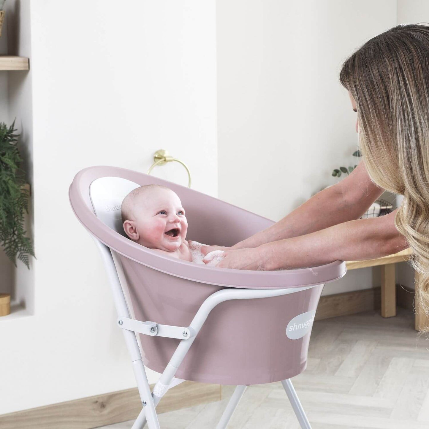 Baby in a pink baby bath seat with a woman in a home setting