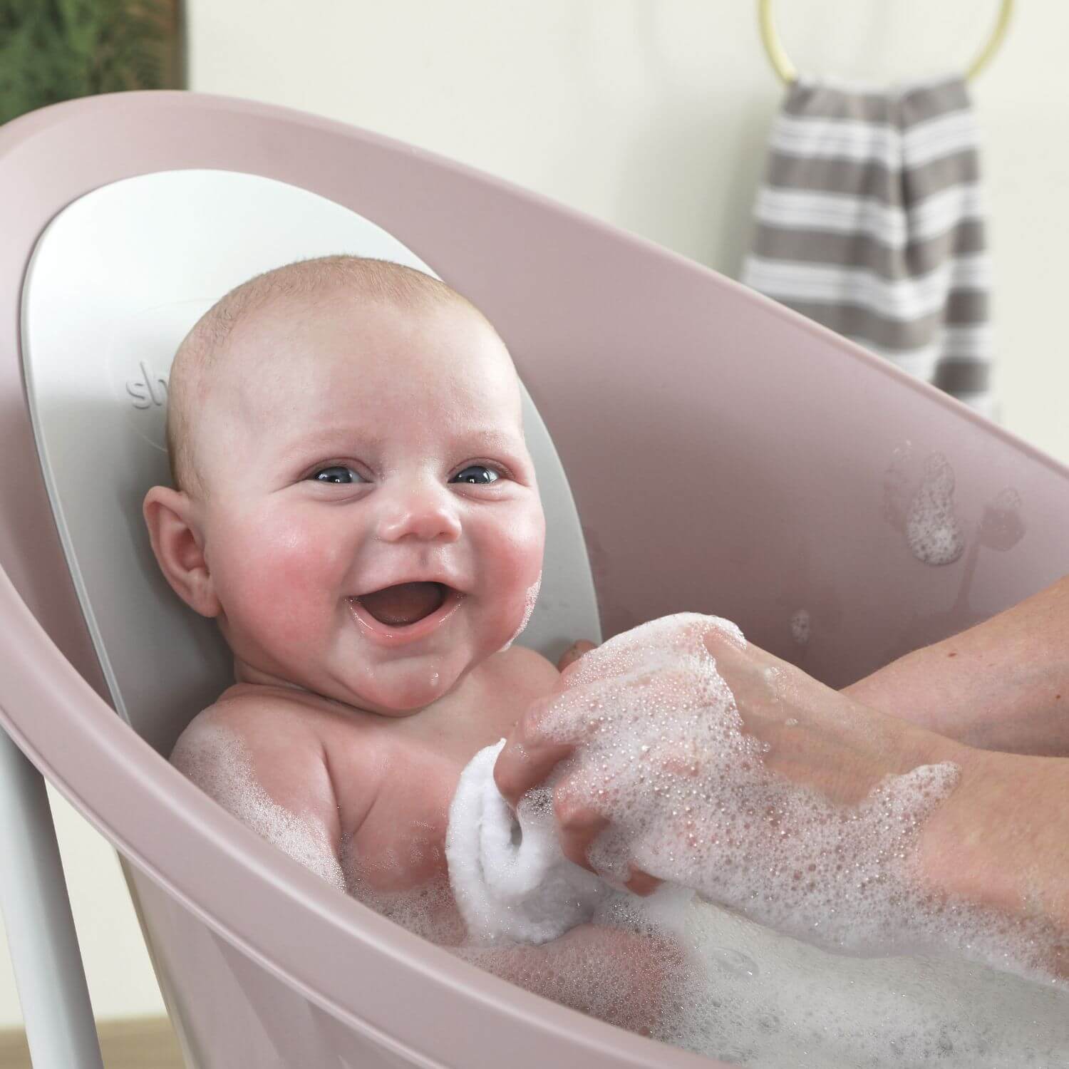 Baby being bathed in a pink baby bathtub with a smiling baby and soapy water.