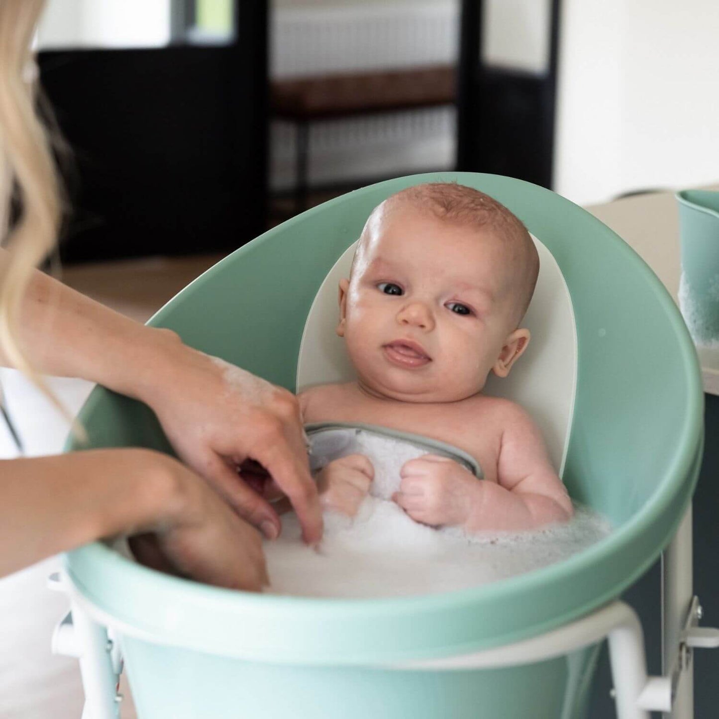 Baby being bathed in a green baby bathtub with a woman's hands.