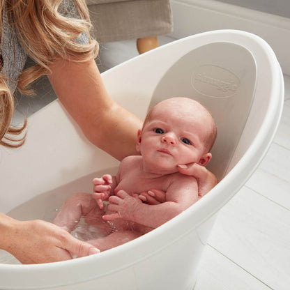 Baby being bathed in a white bathtub by a person.