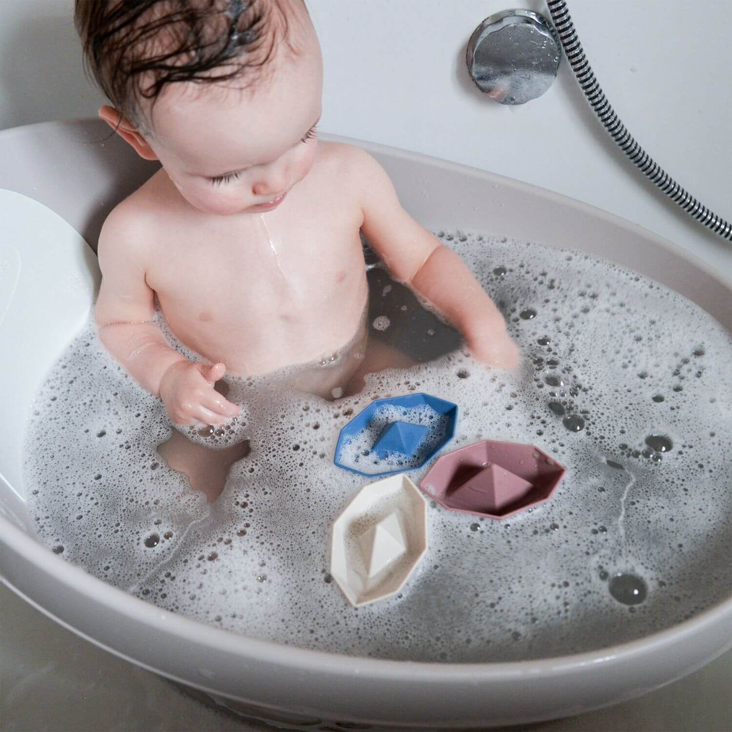 Baby playing with bath toys in a sink filled with soapy water