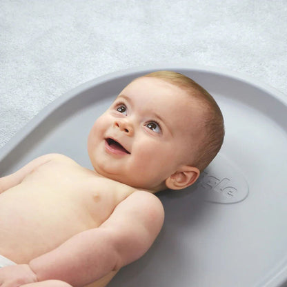 Baby lying on a gray bath seat with a neutral background
