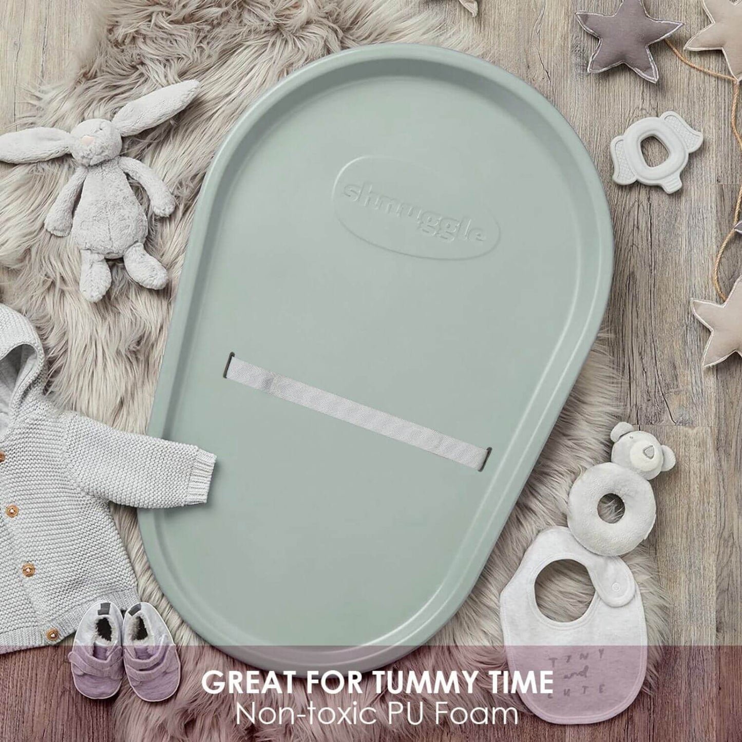 Green baby tray with Smuggle logo on a wooden surface with toys and clothing.