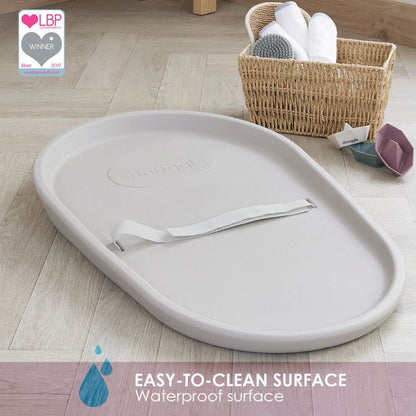 Gray baby changing mat on a wooden floor with a basket of items in the background.