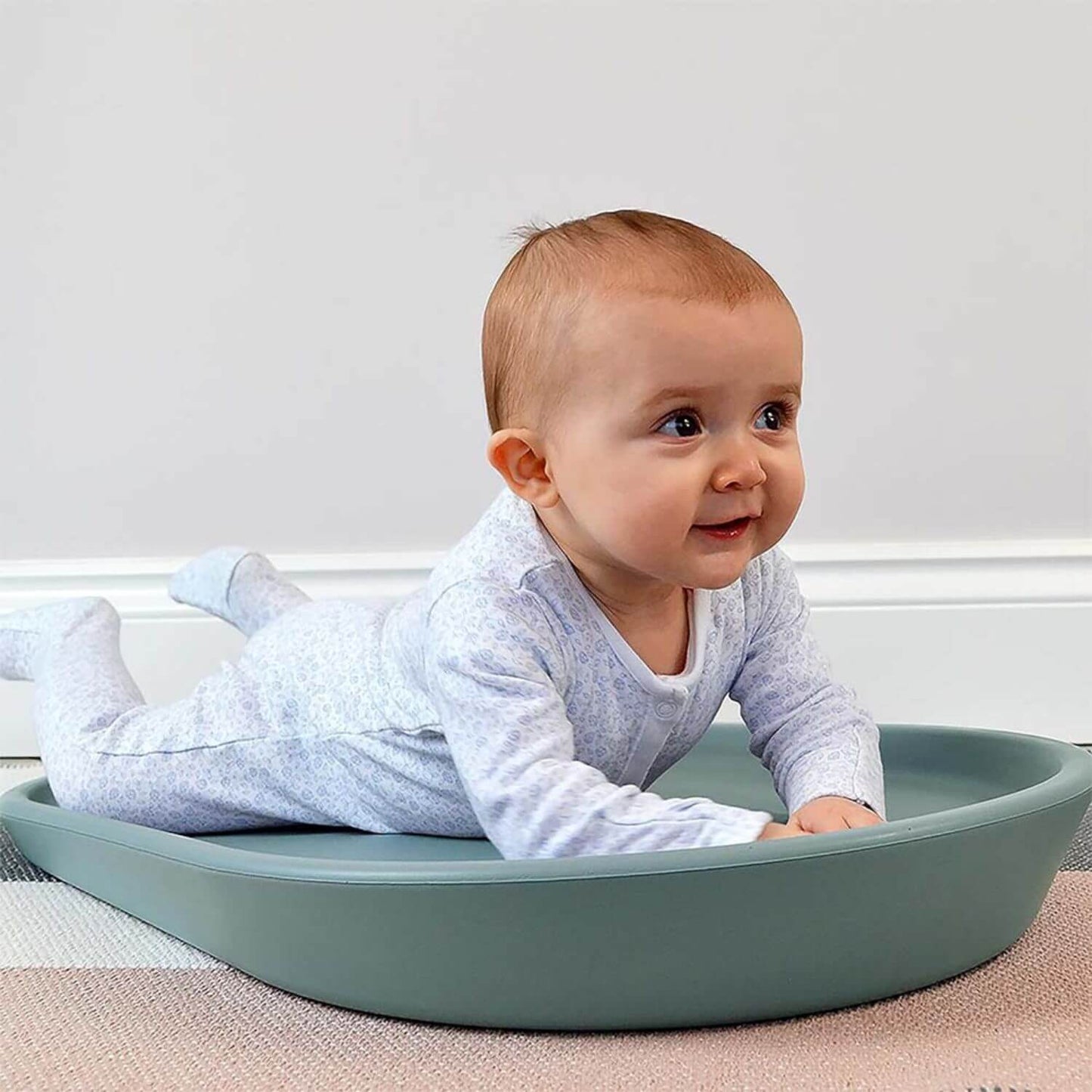 Baby lying in a green playpen with a neutral background
