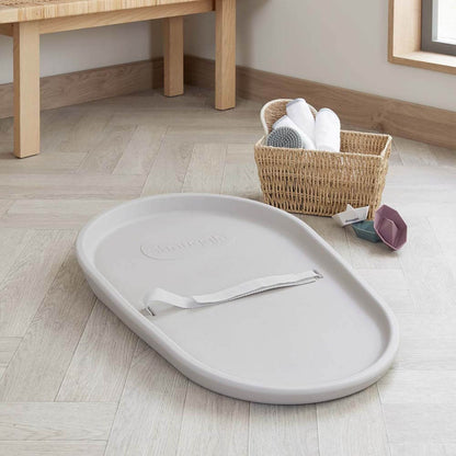 Gray tray with a lid on a wooden floor next to a basket of cleaning supplies.