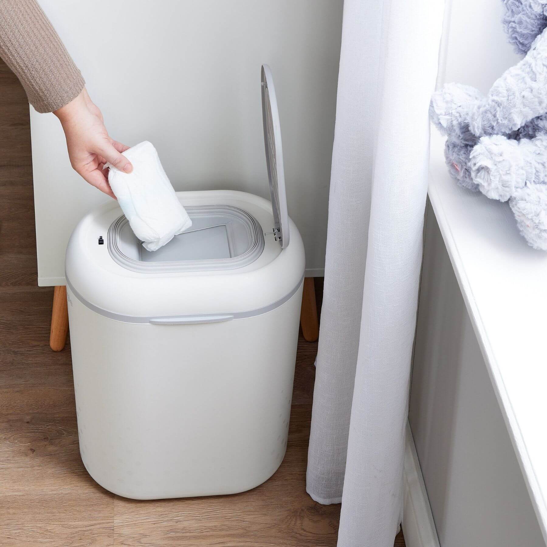 Person disposing of a used diaper into Shnuggle Eco-Touch Nappy Bin Diaper Pail - White in a bathroom setting.
