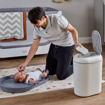 Man changing a baby's diaper next to Shnuggle Eco-Touch Nappy Bin Diaper Pail - White in a home setting.