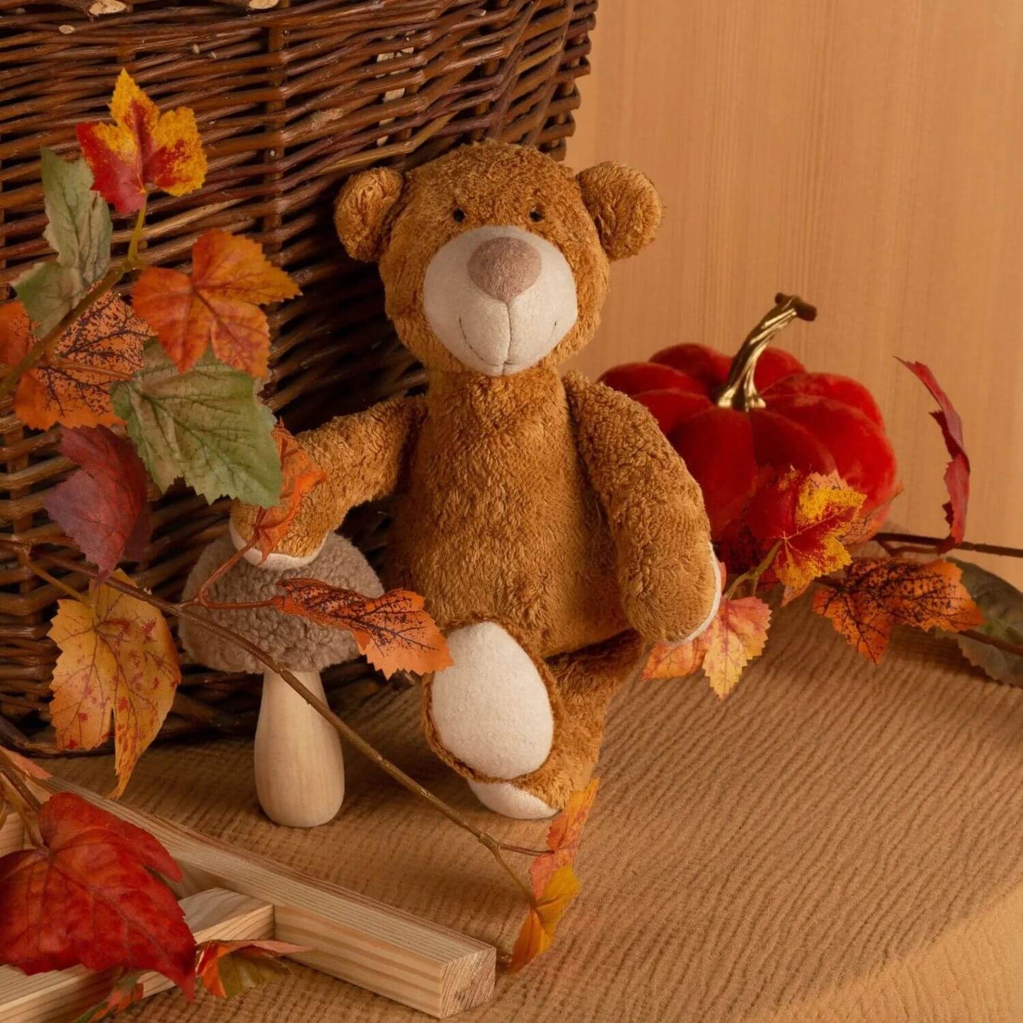 sigikid Organic Bear Cuddle Toy with autumn leaves and a pumpkin on a wooden surface