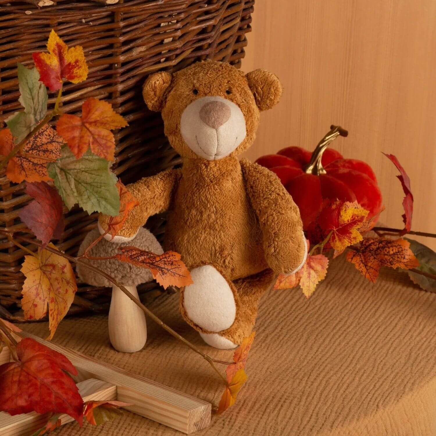sigikid Organic Bear Cuddle Toy with autumn leaves and a pumpkin on a wooden surface
