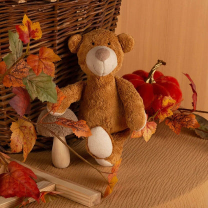 sigikid Organic Bear Cuddle Toy with autumn leaves and a pumpkin on a wooden surface