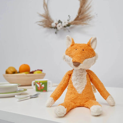 sigikid Organic Plush Fox on a table with a bowl of fruit and decorative items in the background.
