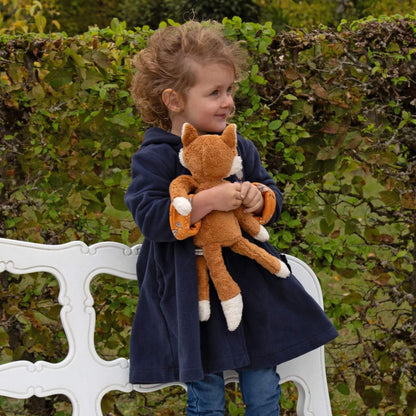 Child holding sigikid Organic Plush Fox outdoors with greenery in the background