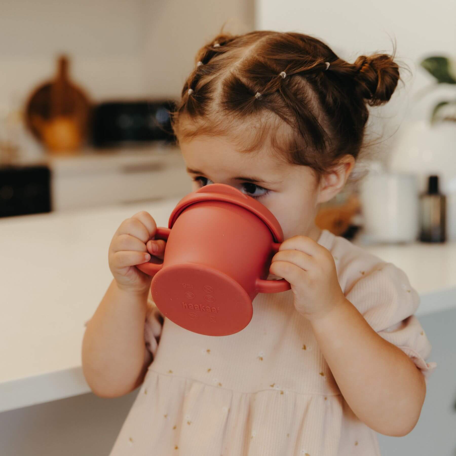 Child drinking from Haakaa Silicone Sip-N-Snack Cup 8 oz in a kitchen setting
