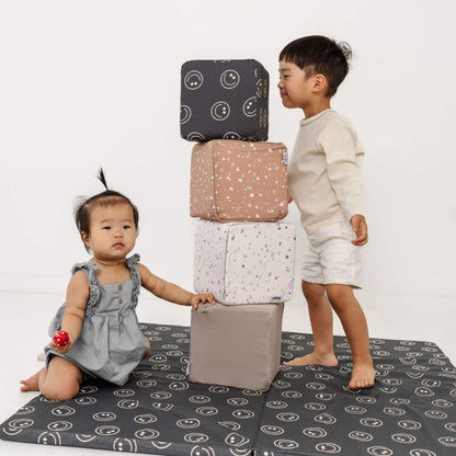 Two children playing with a stack of patterned cushions on a white background