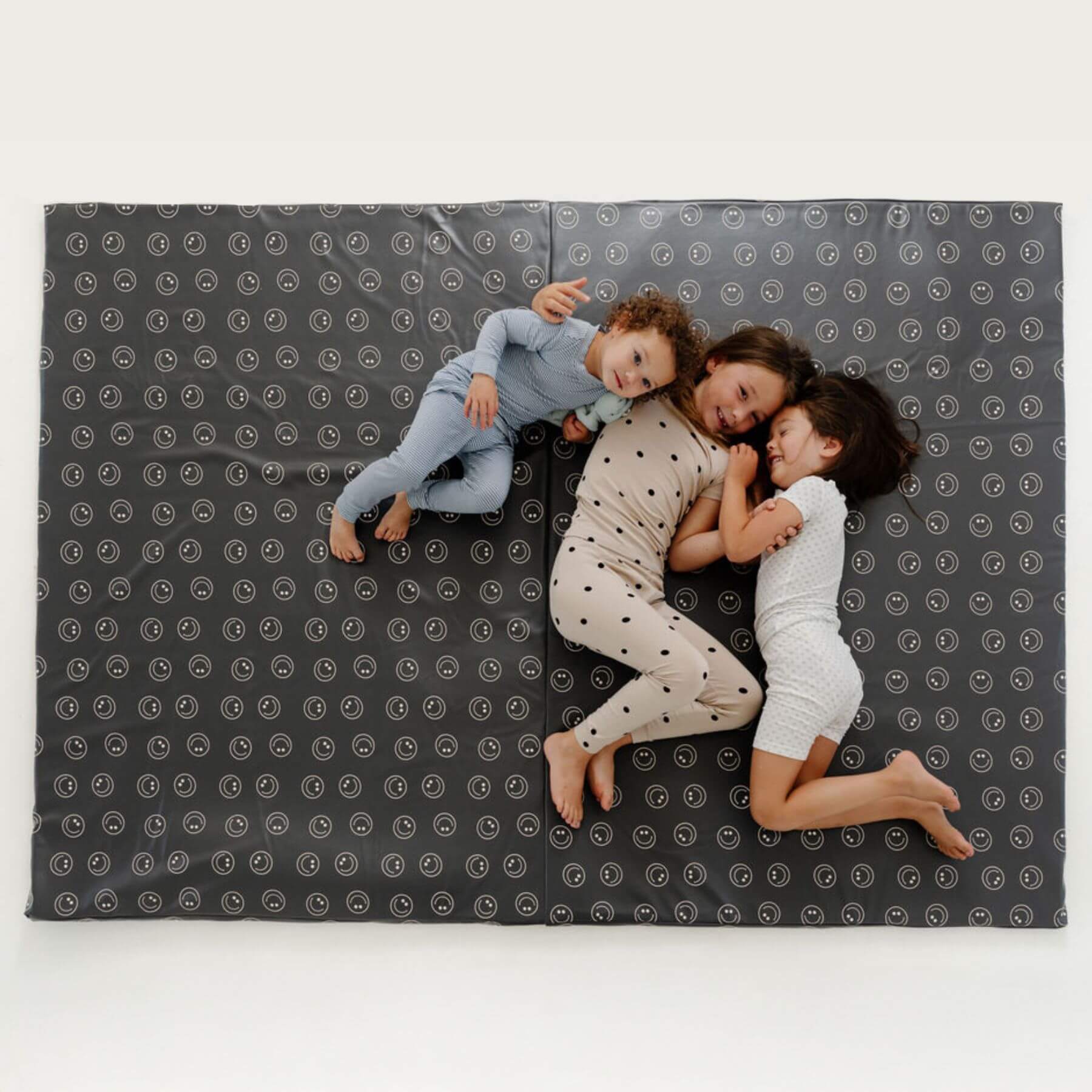 Three children lying on Toki Kids Smiles Vegan Leather Mat