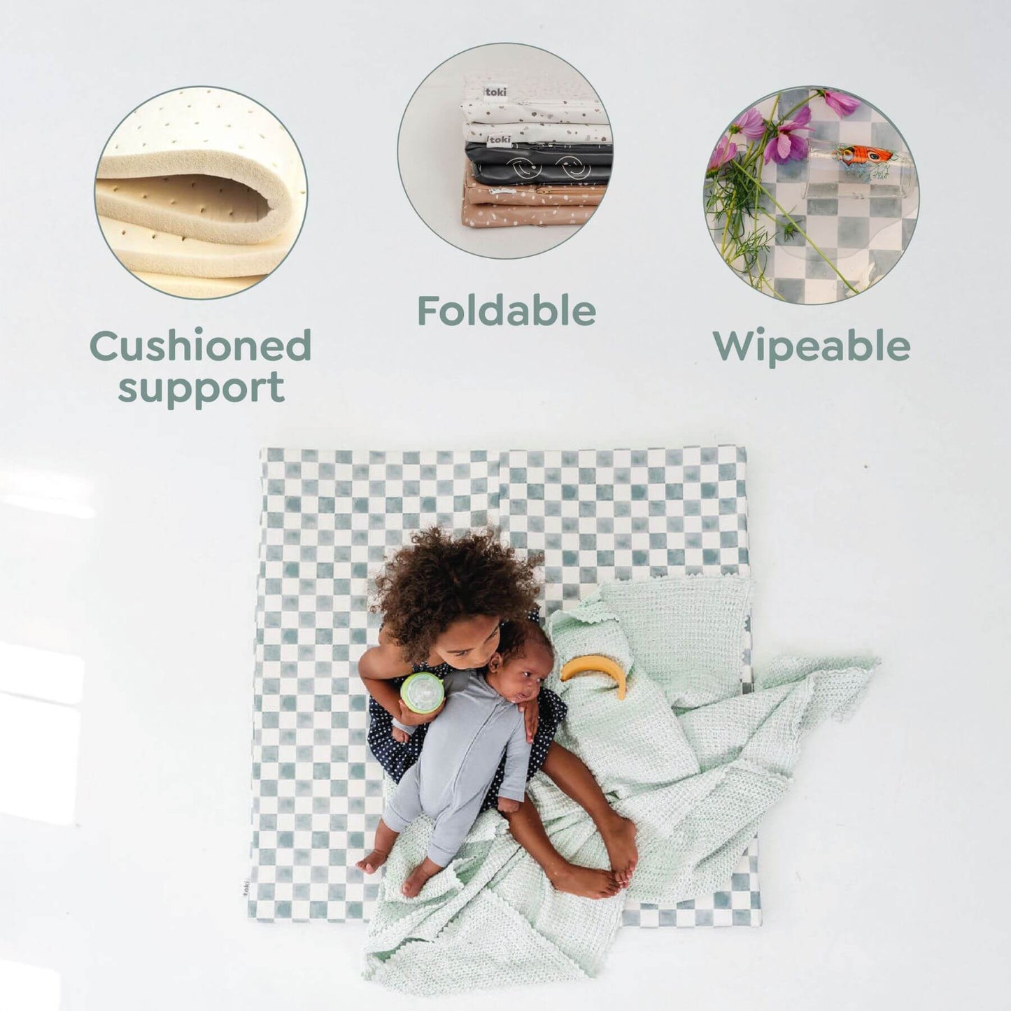 Checkered crib sheet with child on a white background, featuring 'Cushioned support', 'Foldable', and 'Wipeable' text.