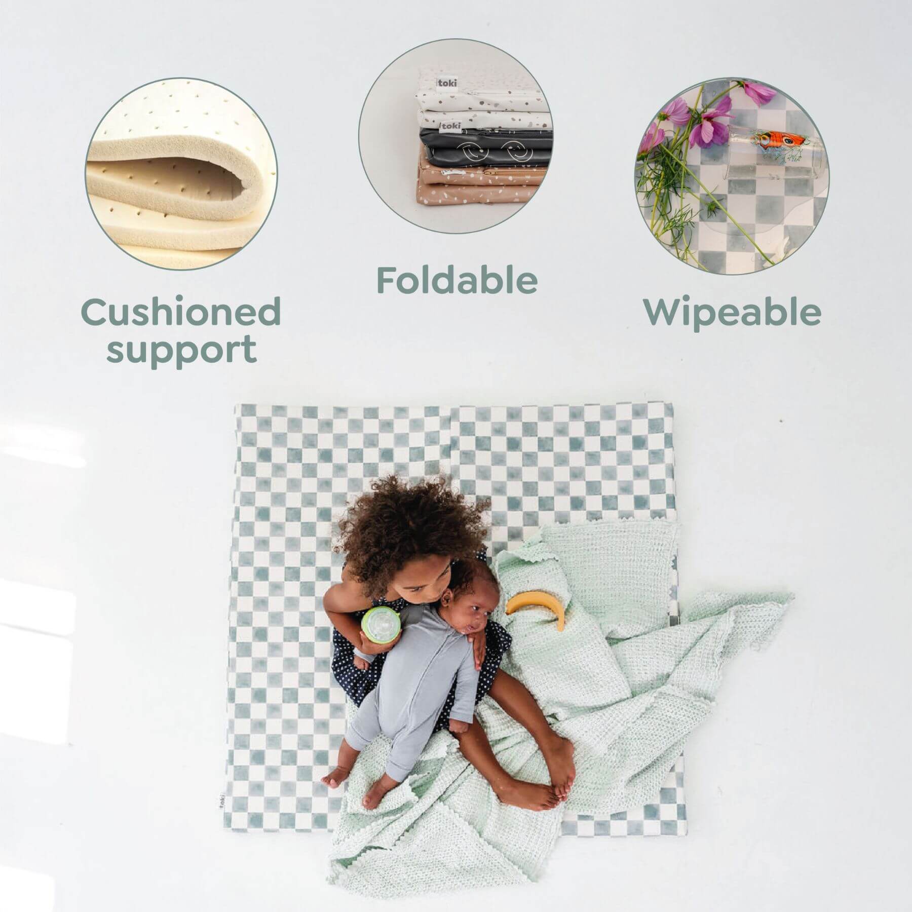Checkered crib sheet with child on a white background, featuring 'Cushioned support', 'Foldable', and 'Wipeable' text.