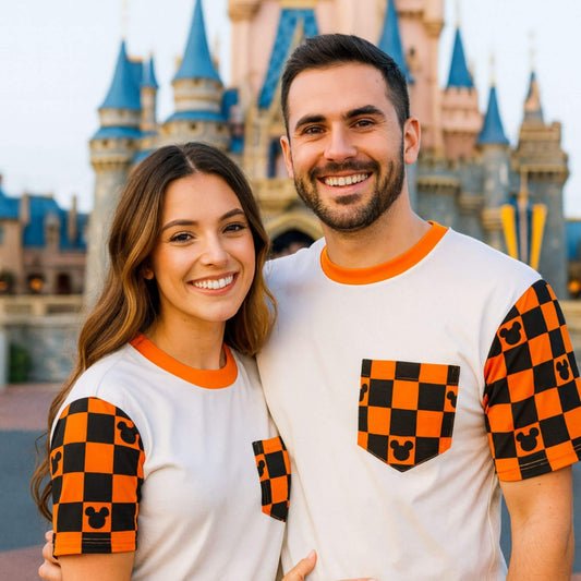 Two people wearing Sweet P Baby Co. Spooky Checkered Magic Adult Pocket Tee in front of a castle.