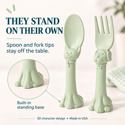 Spoon la la Toddler Utensils — 2-Pack - Green, shown on a light neutral background with marketing text. The spoon has a cat paw design, and the fork has a dog paw design.