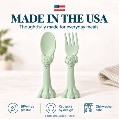 Spoon la la Toddler Utensils — 2-Pack - Green, shaped like cat heads with paw handles. The image features a clean, bright background with text overlays highlighting 'Made in the USA', 'BPA-free plastic', 'Reusable by design', and 'Dishwasher safe'.