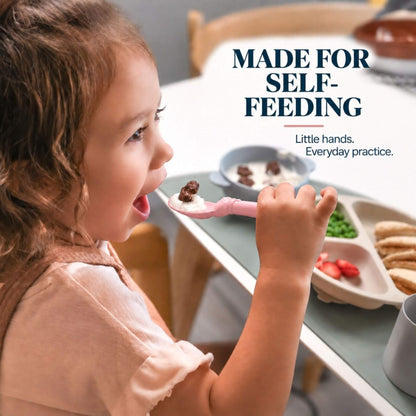 A young child eating from a pink spoon at a high chair table, with the text 'MADE FOR SELF-FEEDING' and 'Little hands. Everyday practice.