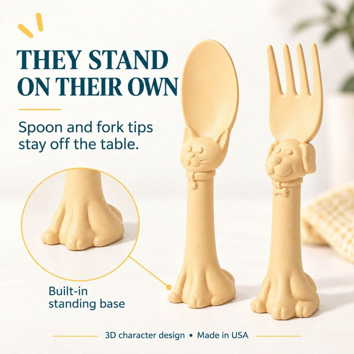 Spoon la la Toddler Utensils — 2-Pack - Yellow, shown standing on their built-in paw bases on a light tabletop. The image includes marketing text explaining that the utensil tips stay off the table and a circular inset showing the paw base detail.
