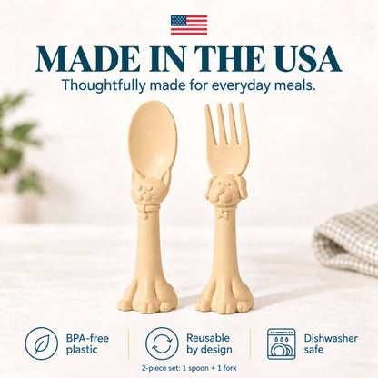 Spoon la la Toddler Utensils — 2-Pack - Yellow, shown on a light tabletop with a soft blurred background. Large text at the top reads 'MADE IN THE USA' with an American flag, and feature icons at the bottom mention BPA-free plastic, reusable by design, and dishwasher safe.