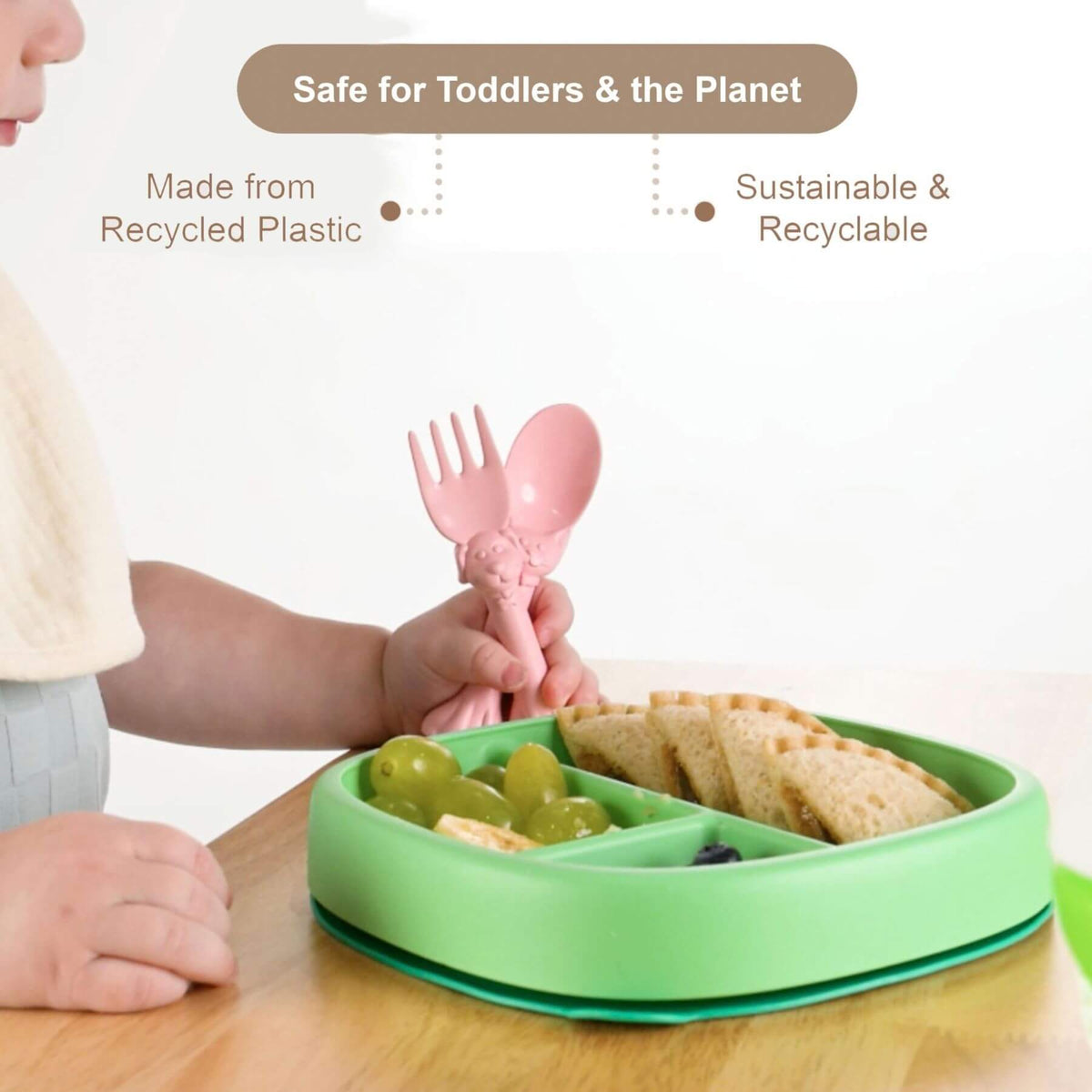 Child using a pink fork over a green divided plate with food on a wooden table, with text about sustainability.