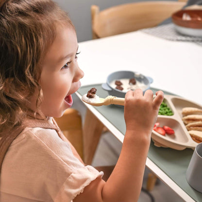 Child eating from a spoon with food at a dining table