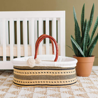 Spring Sparrow No Hood African Moses Basket on a patterned rug next to a white crib and potted plant.