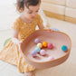 Child playing with colorful balls in a pink bowl on a light-colored floor.