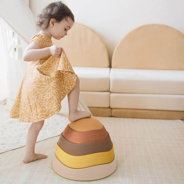 Child in a yellow dress standing on Tiny Land® Stepping Stones - Sunset Hues in a bright room.