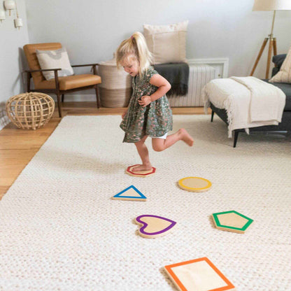 Child playing with Little Partners Step 'N Learn Stepping Stones Shapes on a textured floor in a living room.