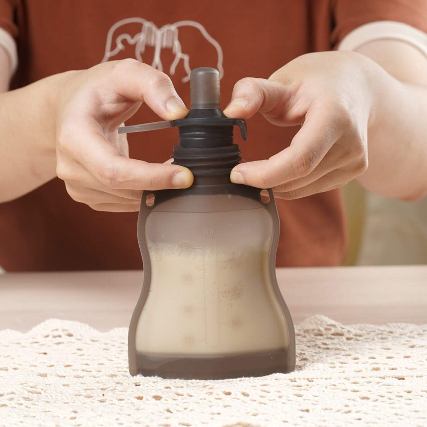 Person using Haakaa Silicone Milk Storage Bag on a textured surface