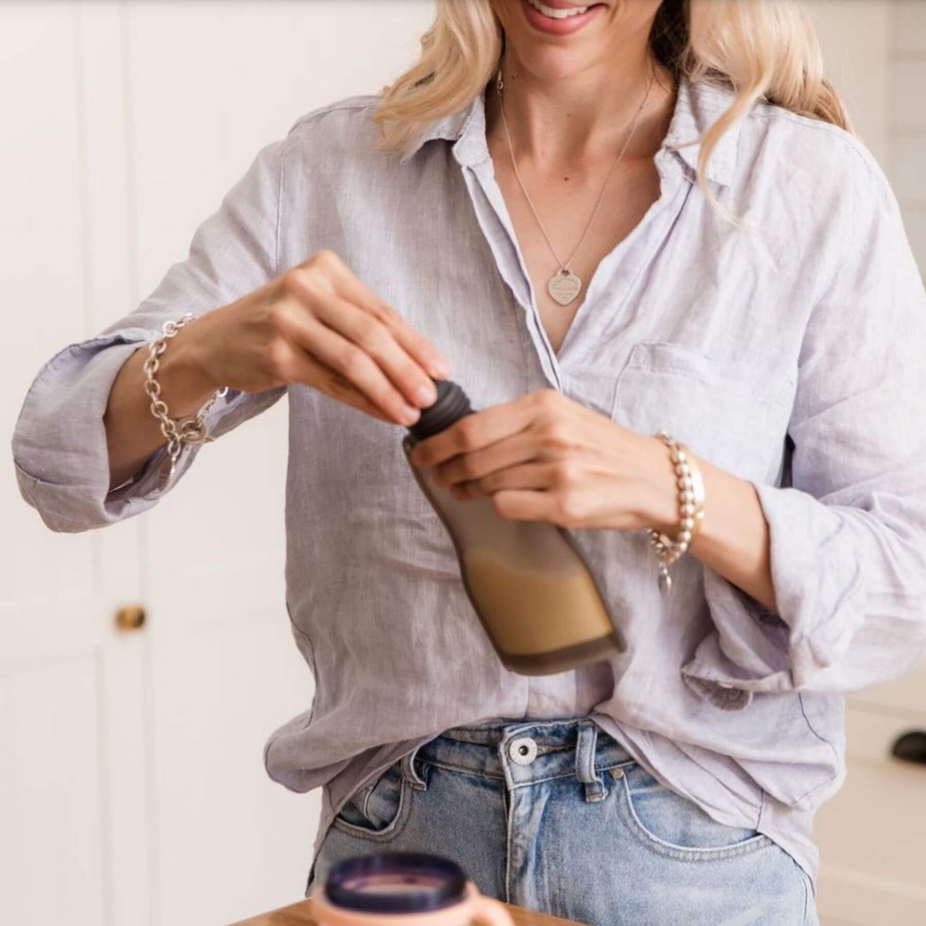 Woman pouring a liquid from a bottle into a container, wearing a light shirt and jeans.