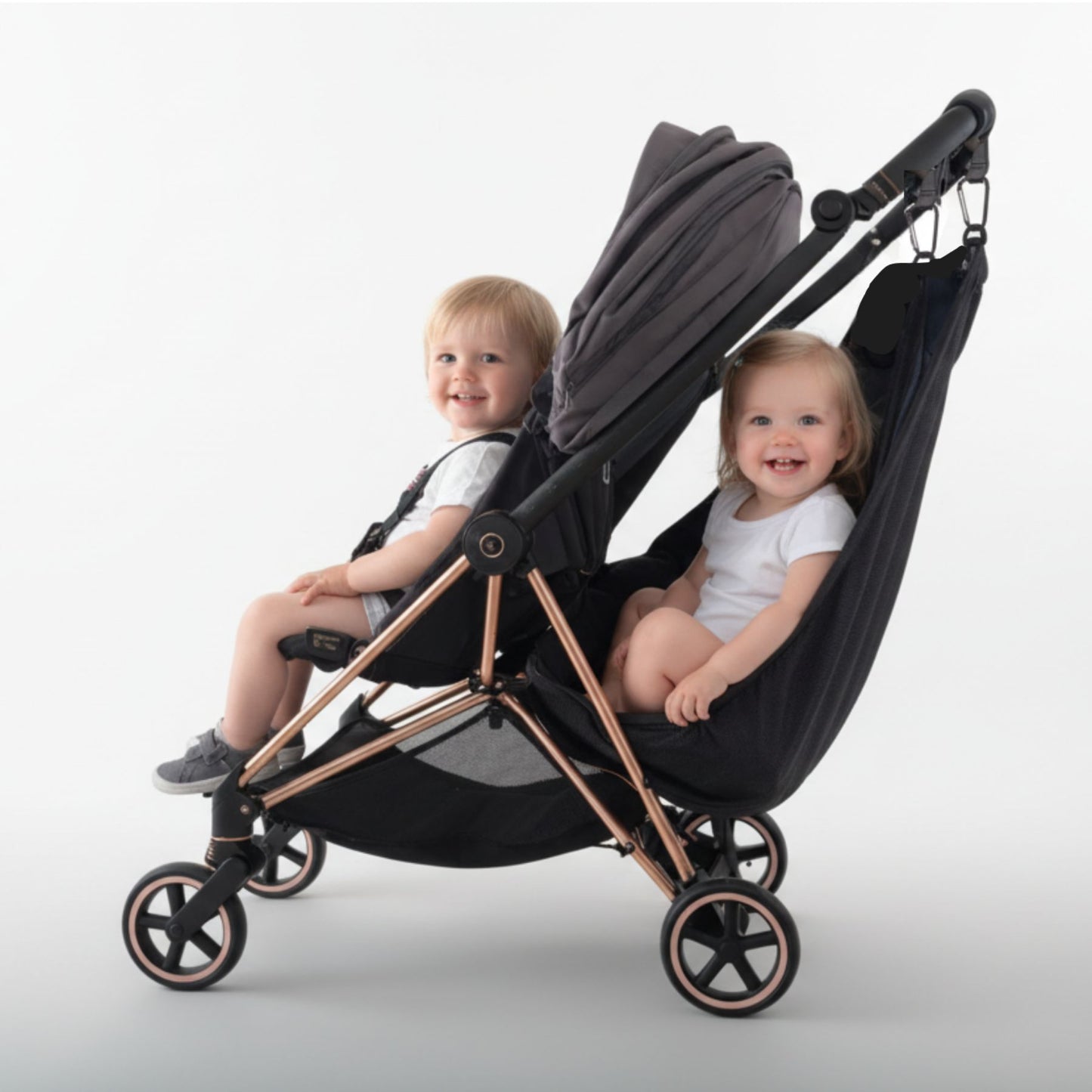 Two children sitting in a black and rose gold stroller with Stroller Sling™ – Black Fox Edition attached