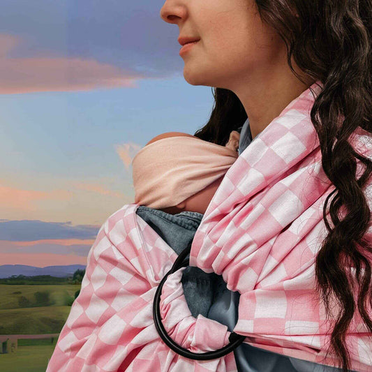 Woman holding a baby in Little Mae & Co Sunkist Ring Sling Carrier against a scenic background