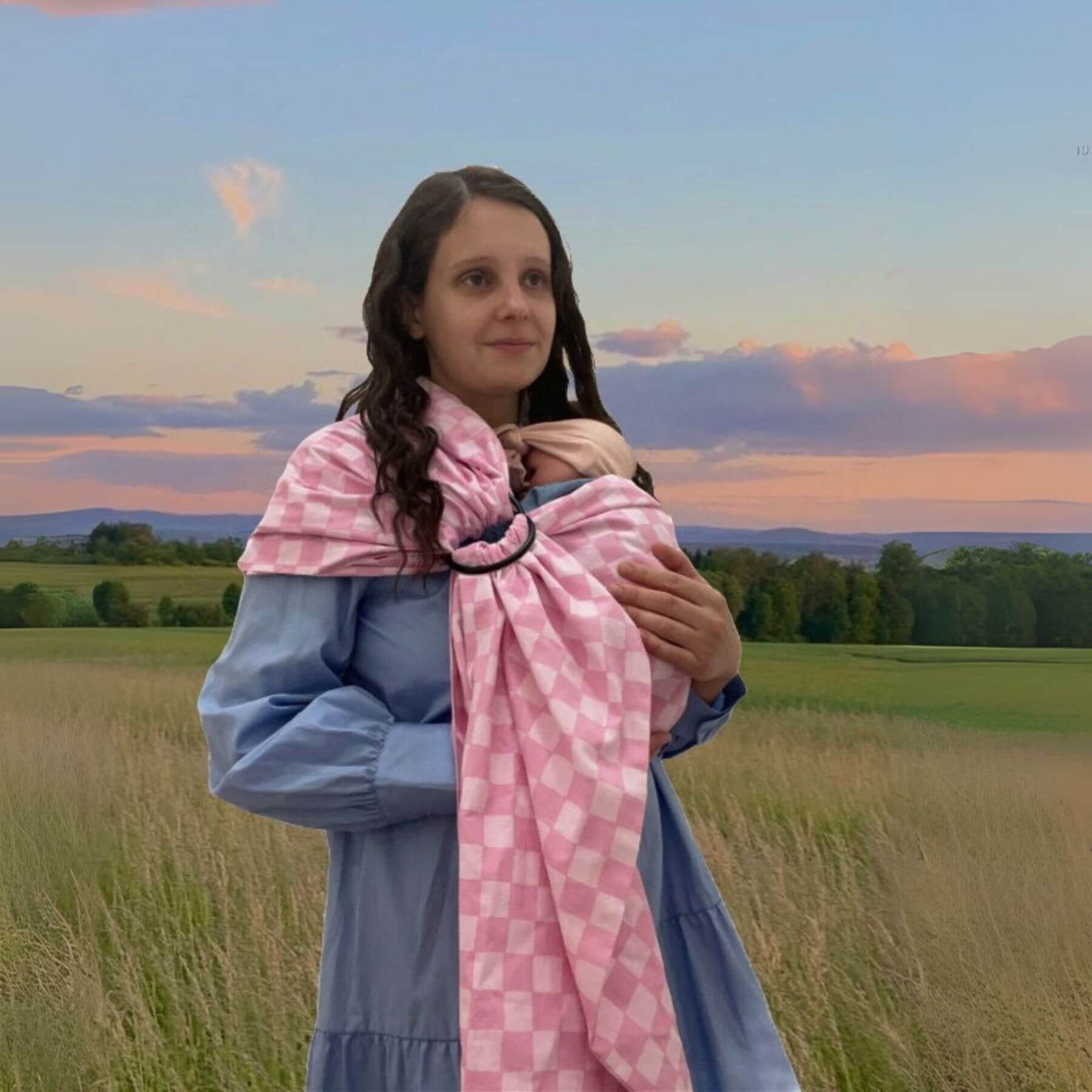 Woman holding a baby in Little Mae & Co Sunkist Ring Sling Carrier against a scenic background