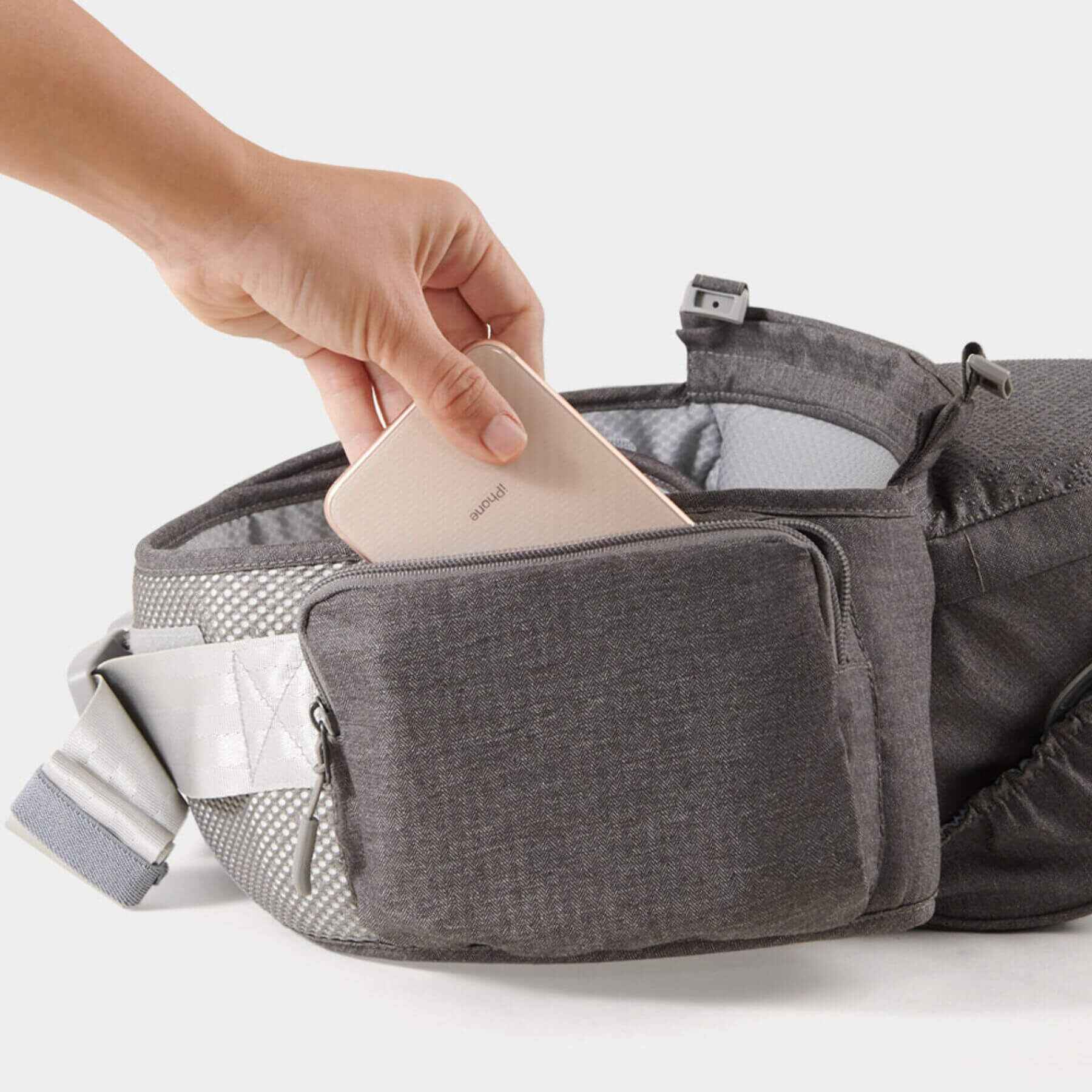 Sunveno Two Shoulder Straps Baby Hipseat with a hand placing a phone into one of its pockets on a white background