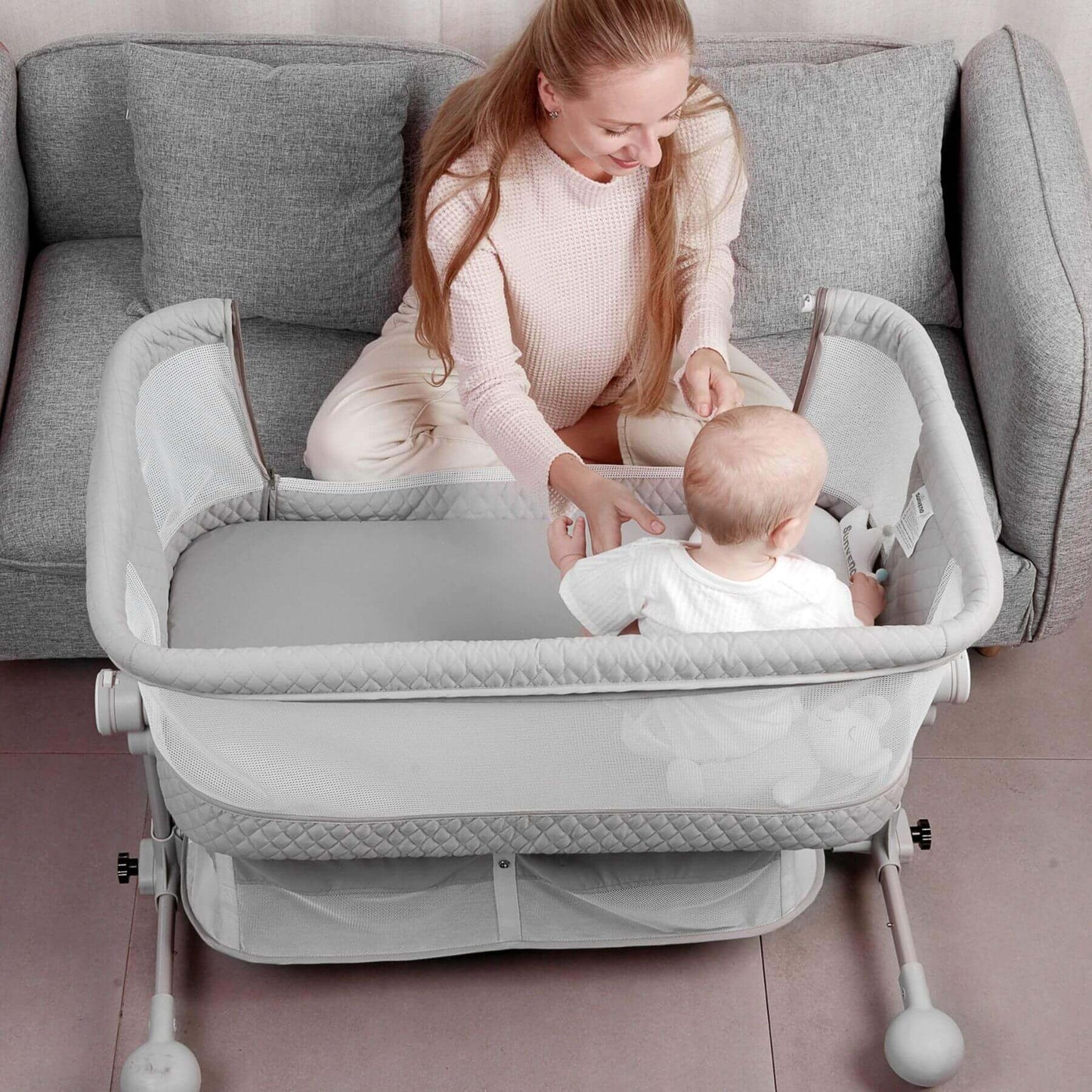 Woman sitting with a baby in Sunveno Baby Bassinet Bedside Crib in a living room.