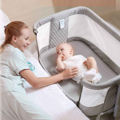 Woman holding a baby in Sunveno Baby Bassinet Bedside Crib next to a bed