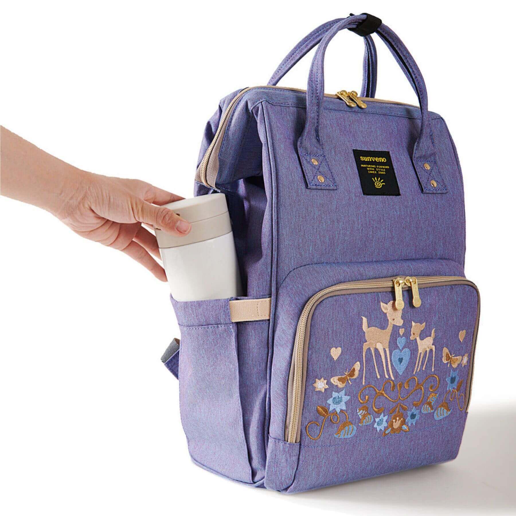 Sunveno Classic Embroidered Diaper Backpack - Purple Deer and a hand placing a cup inside on a white background