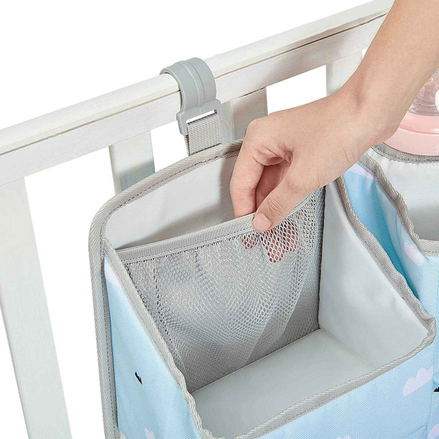 Handy storage bag attached to a crib with a hand reaching in.