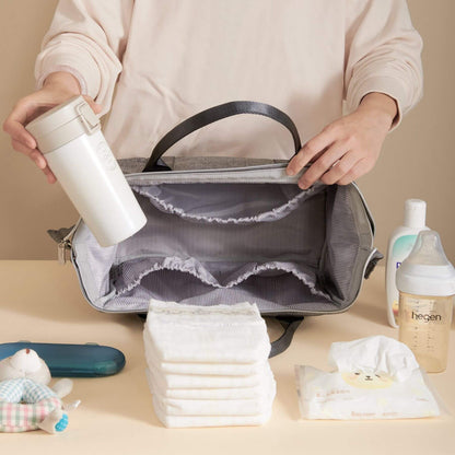 Person organizing Sunveno Small Crossbody Diaper Bag with baby items on a beige surface