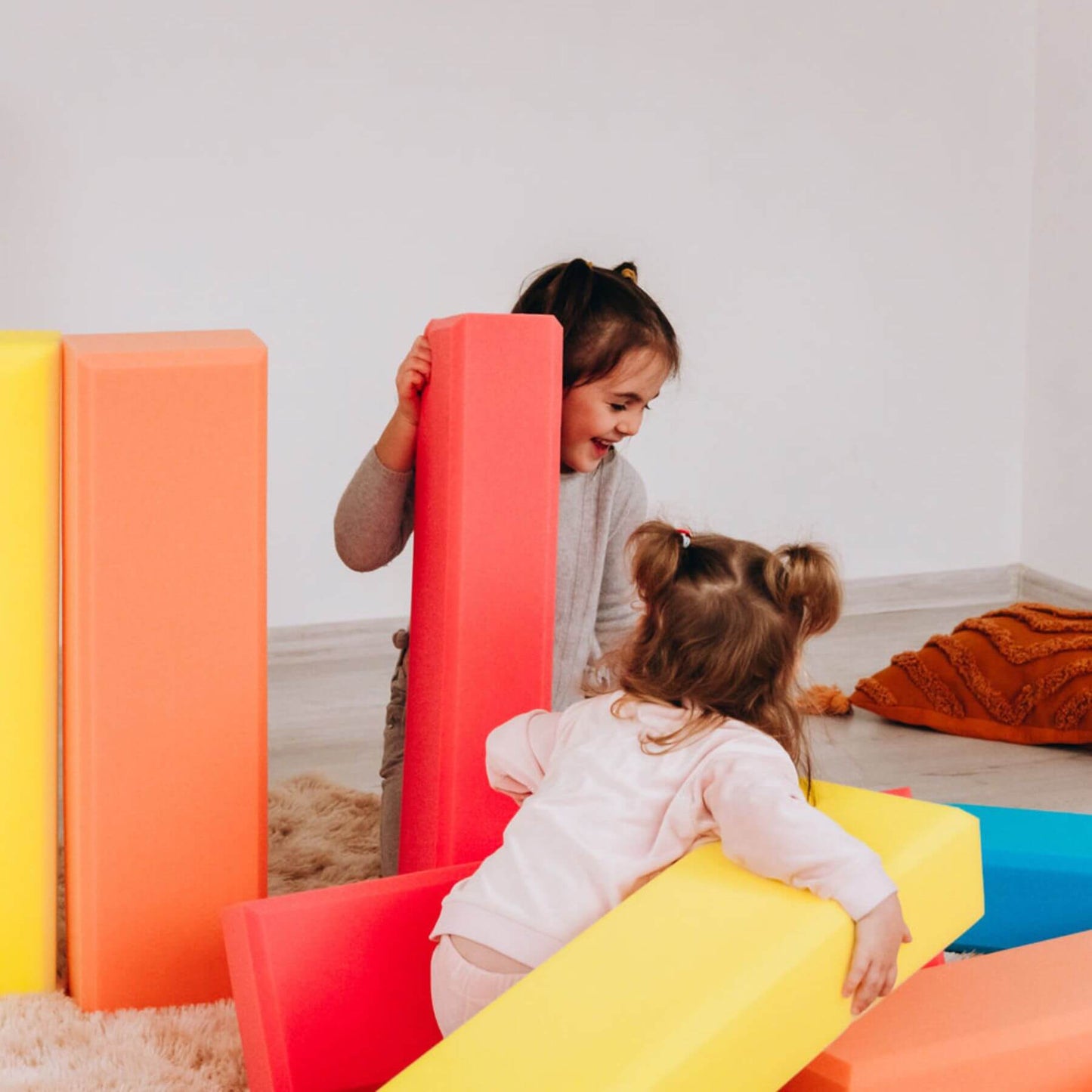 Two children playing with colorful soft play structures indoors.