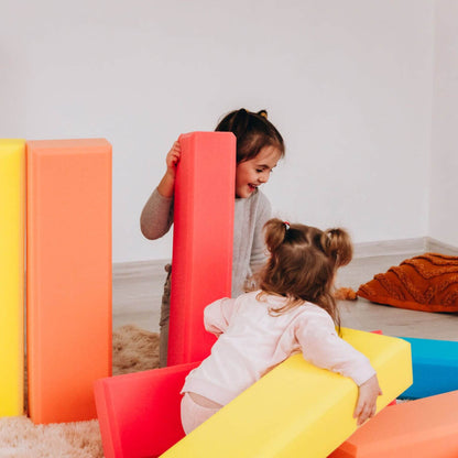 Two children playing with colorful soft play structures indoors.